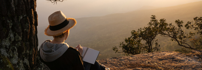 Woman sitting on hillside with book.